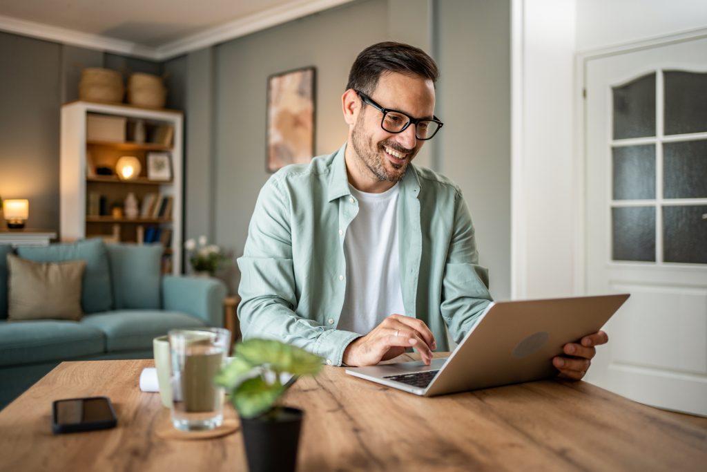 Portrait of handsome Caucasian man looking at laptop, working online from his home