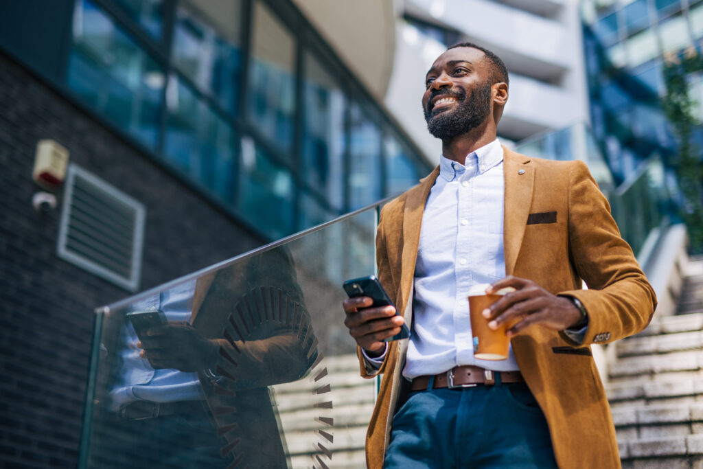 an adult handsome black businessman outside of corporation, using phone