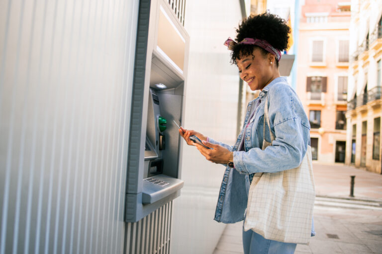 Happy multiracial woman using a mobile app and taking the money from the ATM