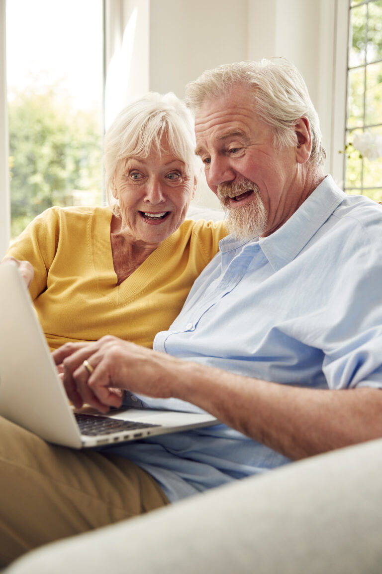 Retired Senior Couple Sitting On Sofa At Home Using Laptop
