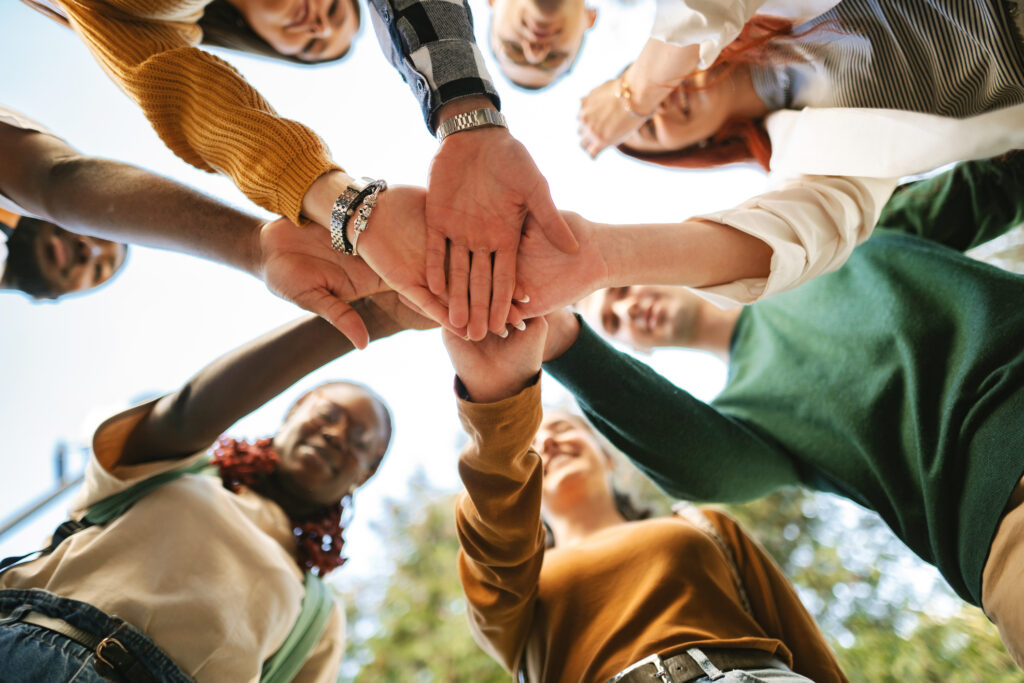 A diverse group of students unites in a collaborative circle, showcasing friendship and teamwork under the sunny campus sky