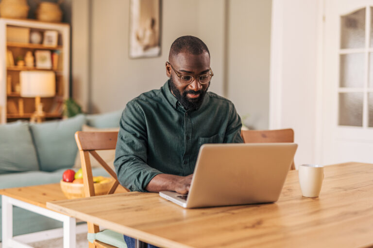 Focused black man working from home on laptop at dining table