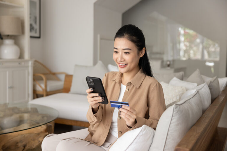 Smiling Asian woman doing online shopping using card and smartphone
